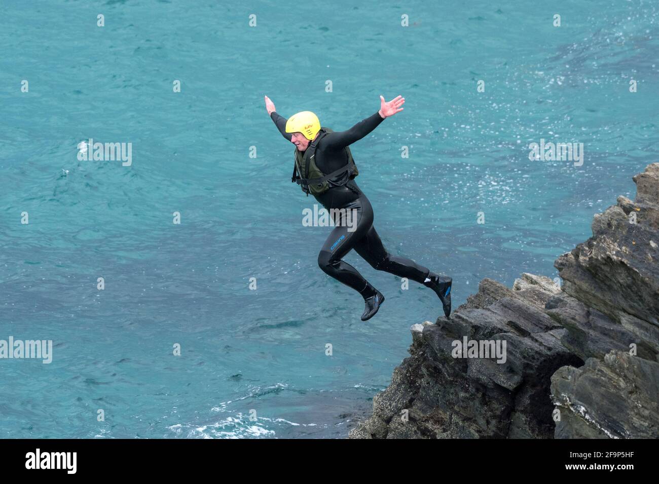 Un turista che si allena in mare dalle rocce in un viaggio di coastering intorno a Towan Head a Newquay in Cornovaglia. Foto Stock