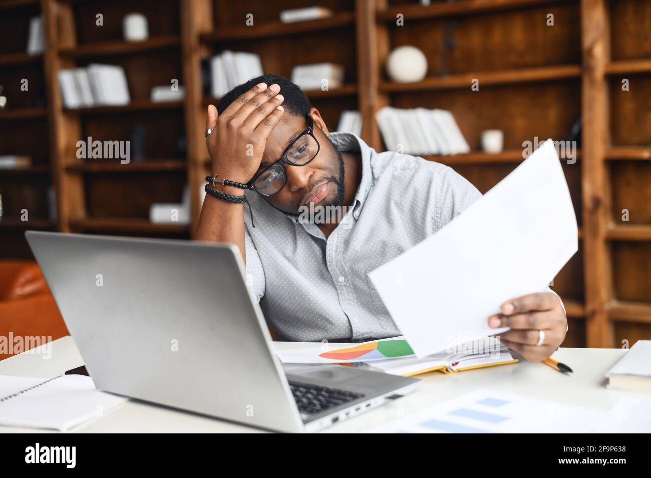 Dispiaciuto afroamericano uomo guardando attraverso i documenti di lavoro, ha sottolineato nero maschile dipendente lettura di un documento di dichiarazione bancaria seduta in ufficio, ha cattivo equilibrio, fallimento, debito Foto Stock