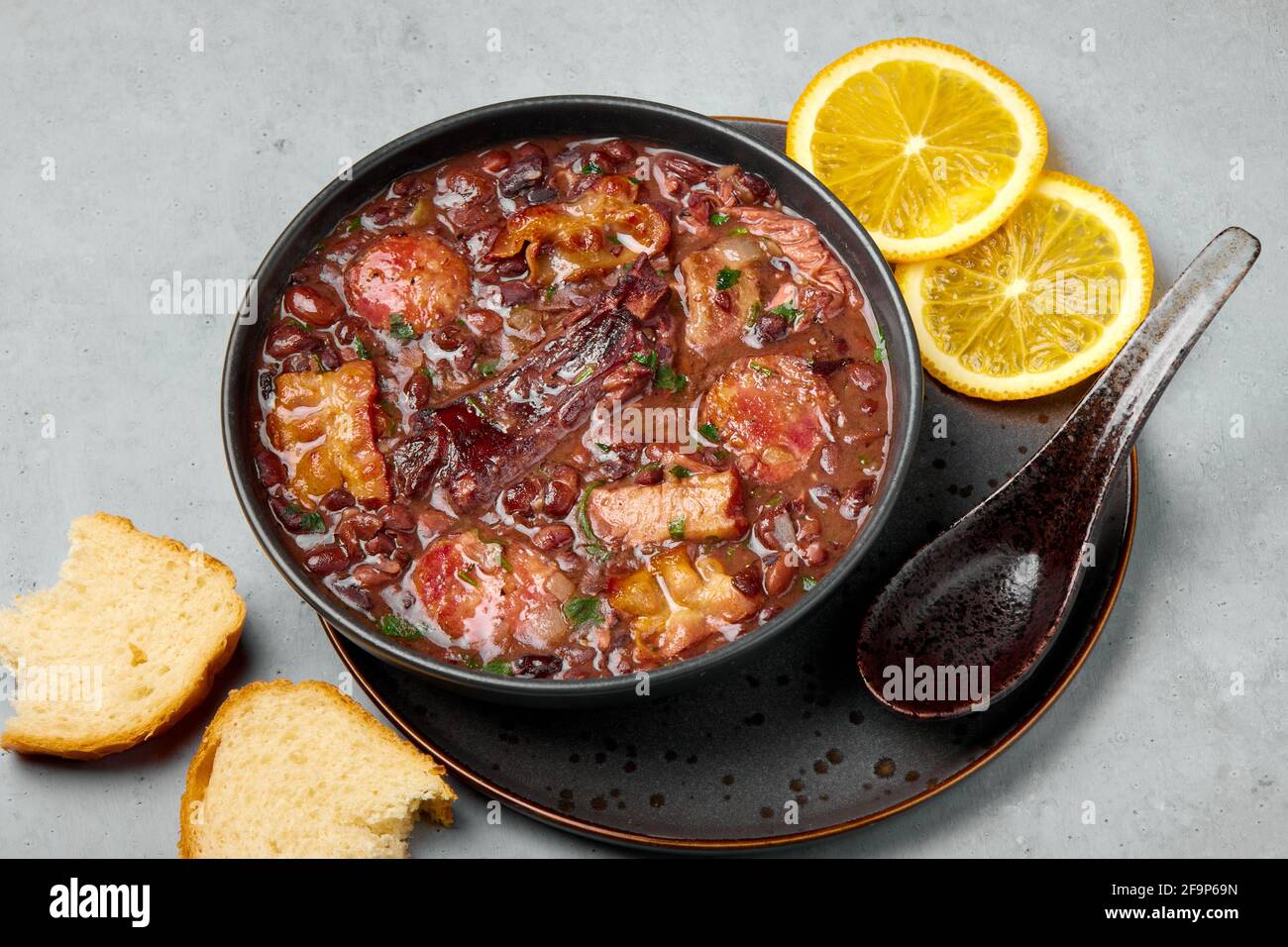 Feijoada in nero ciotola grigio tavolo. Cucina brasiliana e portoghese tradizionale fagioli stufato di carne Foto Stock