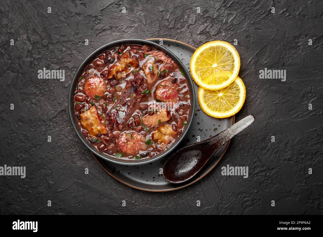 Feijoada in ciotola nera su piano tavolo in ardesia scura. Cucina brasiliana e portoghese tradizionale fagioli stufato di carne Foto Stock