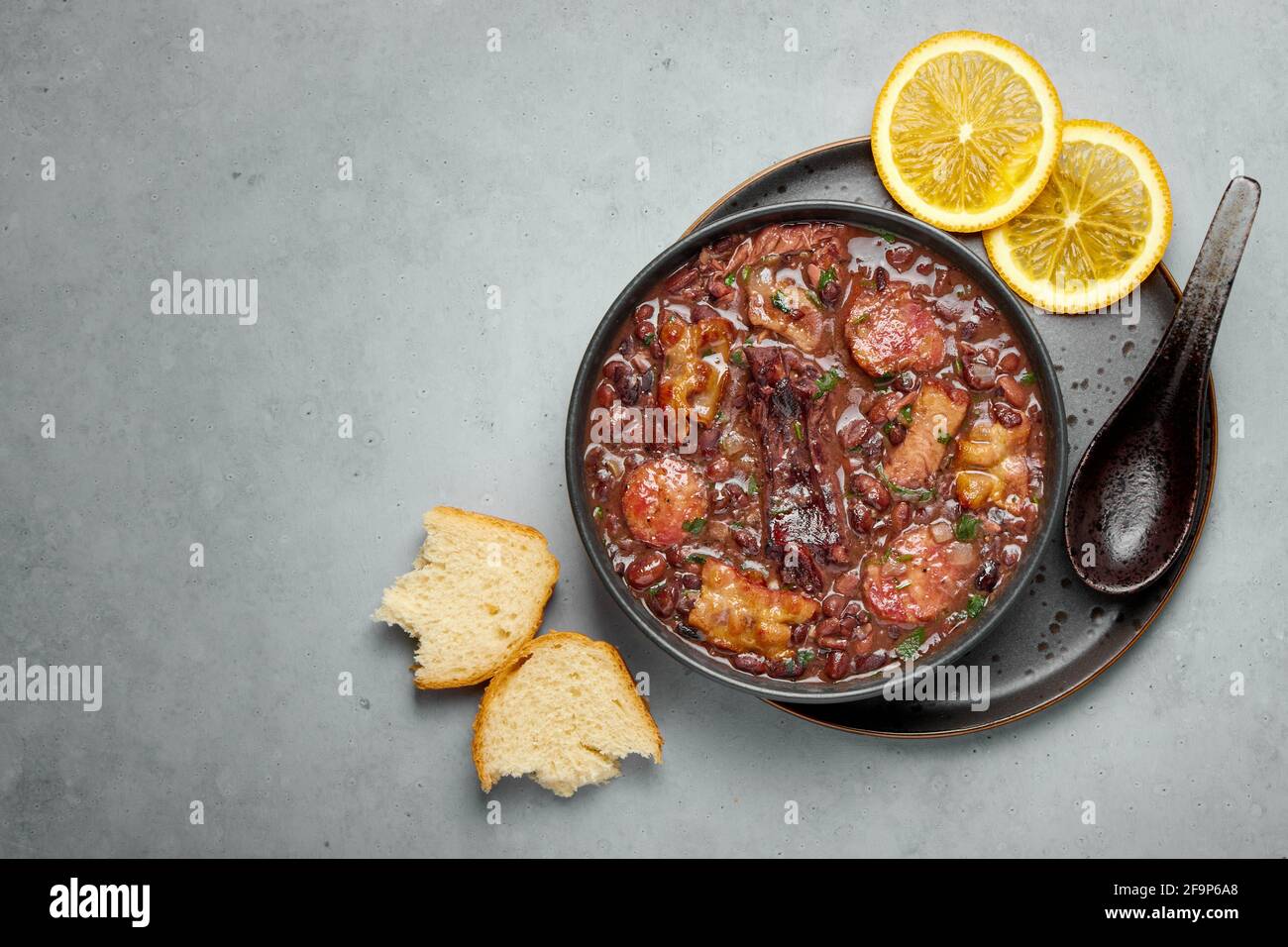 Feijoada in nero ciotola grigio tavolo. Cucina brasiliana e portoghese tradizionale fagioli stufato di carne Foto Stock