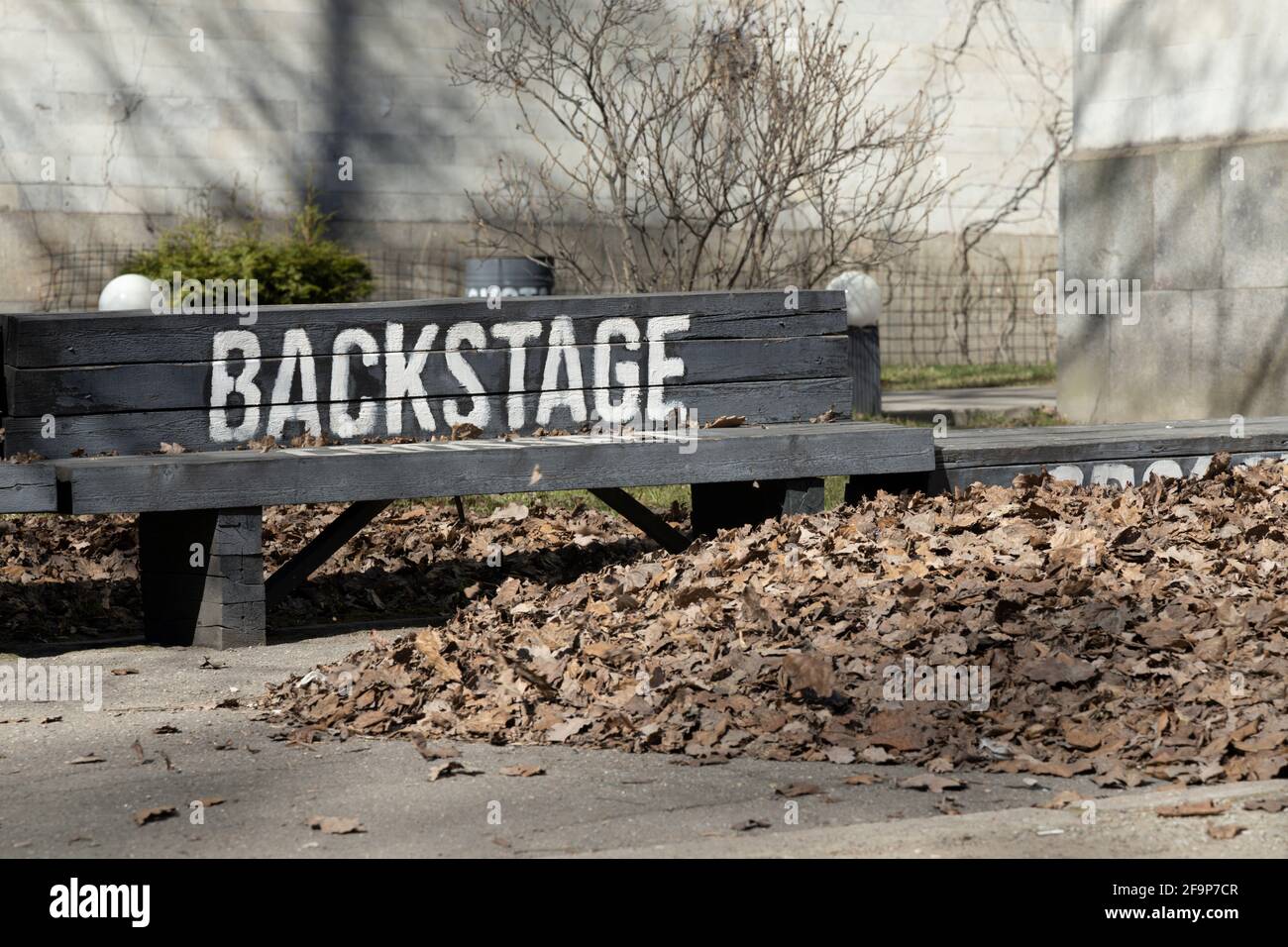 Panca nera con un'iscrizione bianca 'backstage' accanto ad A. mucchio grande di foglie secche cadute Foto Stock