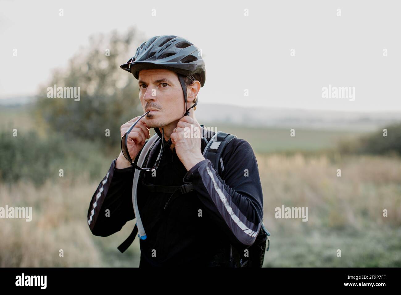 Uomo che indossa abbigliamento sportivo che indossa il casco. Ciclista maschio che fissa la cinghia dell'elmetto prima di partire per il trekking in bicicletta. Foto Stock