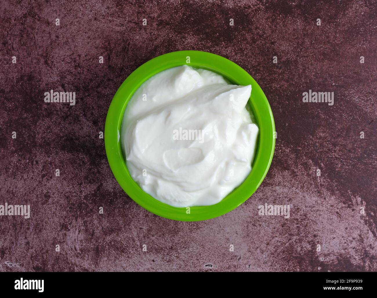 Vista dall'alto di una piccola ciotola verde riempita di yogurt greco puro su un piano del marron. Foto Stock