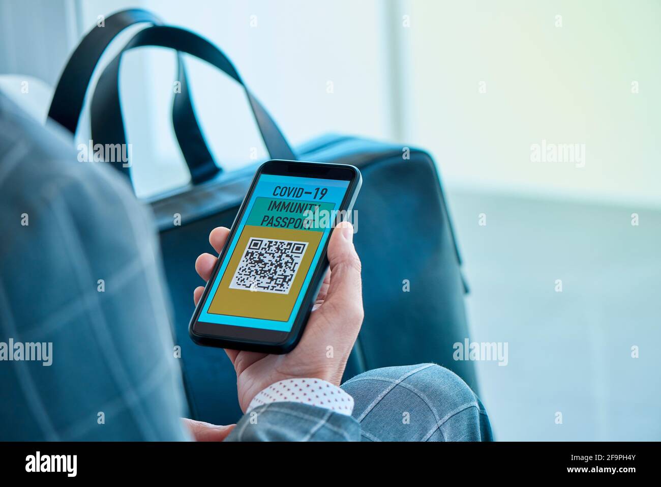 closeup di un giovane uomo d'affari caucasico, indossando un elegante abito grigio, con un copid elettronico simulato-19 passaporto immunità nel suo smartphone, si Foto Stock