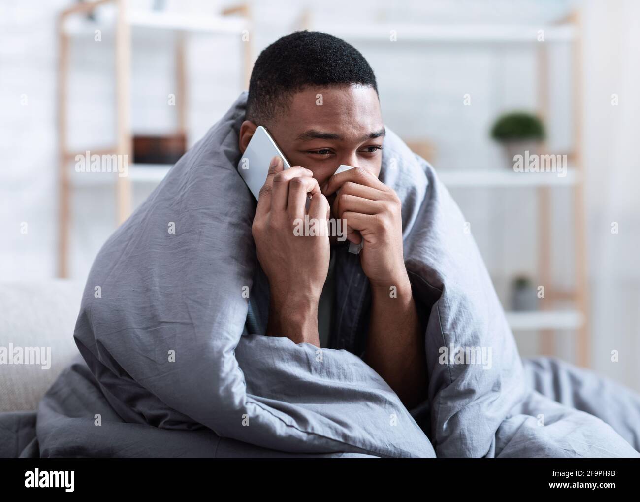 L'uomo nero malato che chiama Dottore avendo naso che cola seduto all'interno Foto Stock