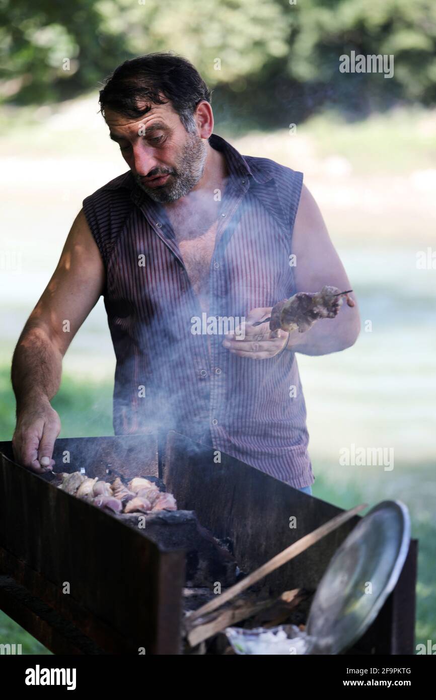 17.07.2018, Keda, Ajaria, Georgia - uomo che grigliano i kebab di carne su una griglia di carbone in un parco. 00S180717D039CAROEX.JPG [VERSIONE DEL MODELLO: NO, RELEDA PROPRIETÀ Foto Stock