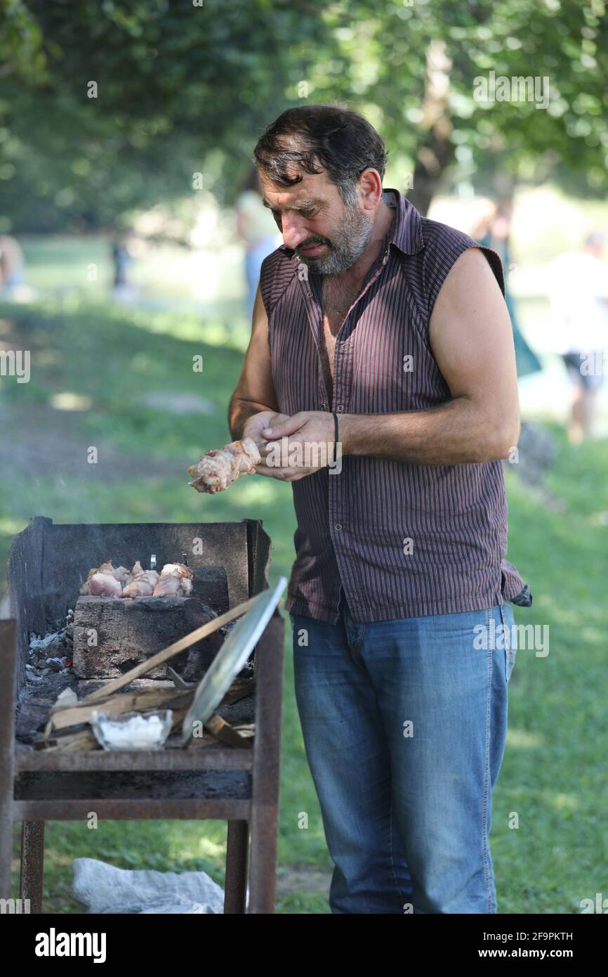 17.07.2018, Keda, Ajaria, Georgia - uomo grigliare spiedini di carne su una griglia a carbone in un parco. 00S180717D038CAROEX.JPG [RELEASE DEL MODELLO: NO, PROPERTY RELE Foto Stock