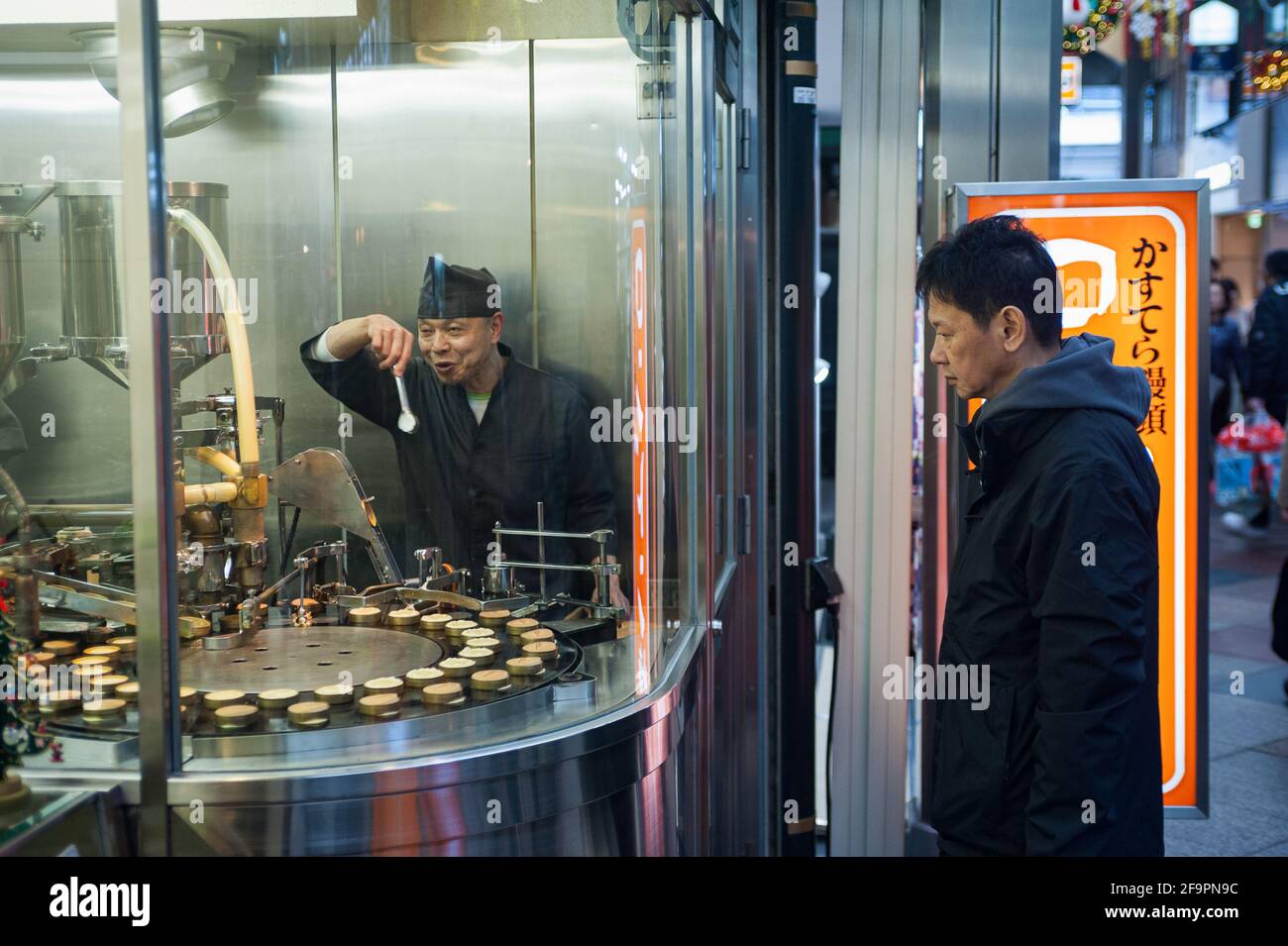 25.12.2017, Kyoto, Kansai, Giappone - UN uomo si erge davanti alla finestra di una pasticceria e guarda la produzione di biscotti. 0SL171225D031CAROEX.JP Foto Stock