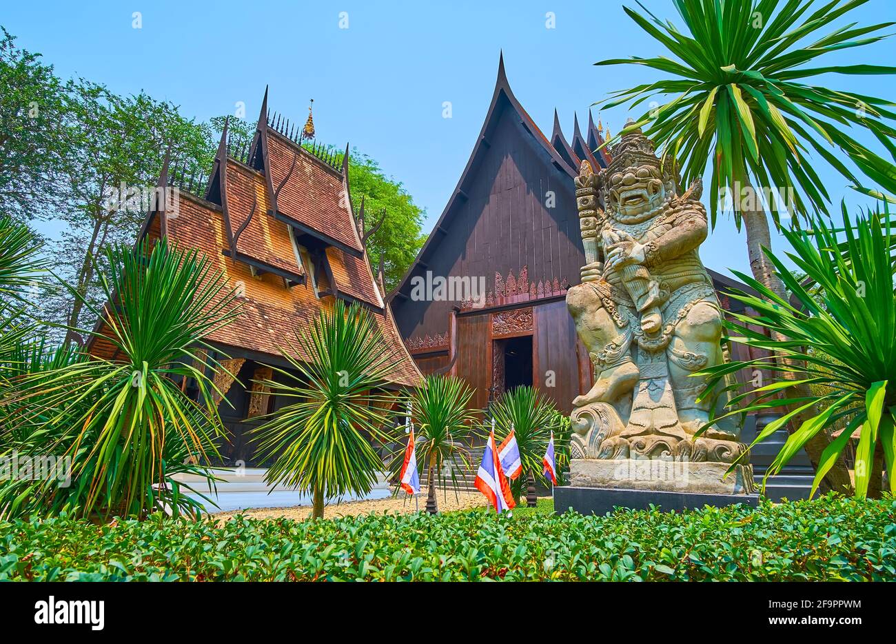 CHIANG RAI, THAILANDIA - 11 MAGGIO 2019: Il giardino ornamentale con yucche, scultura in pietra della guardia di Yaksha e la Sala principale del Santuario della Casa Nera Foto Stock