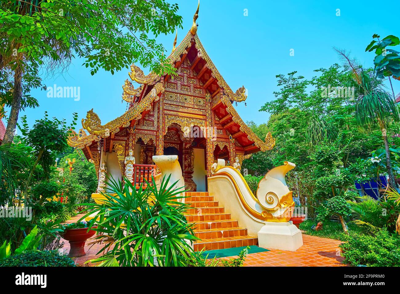 L'edificio medievale ornato del Viharn di Wat Phra Singh, circondato da un lussureggiante giardino tropicale, Chiang Rai, Thailandia Foto Stock
