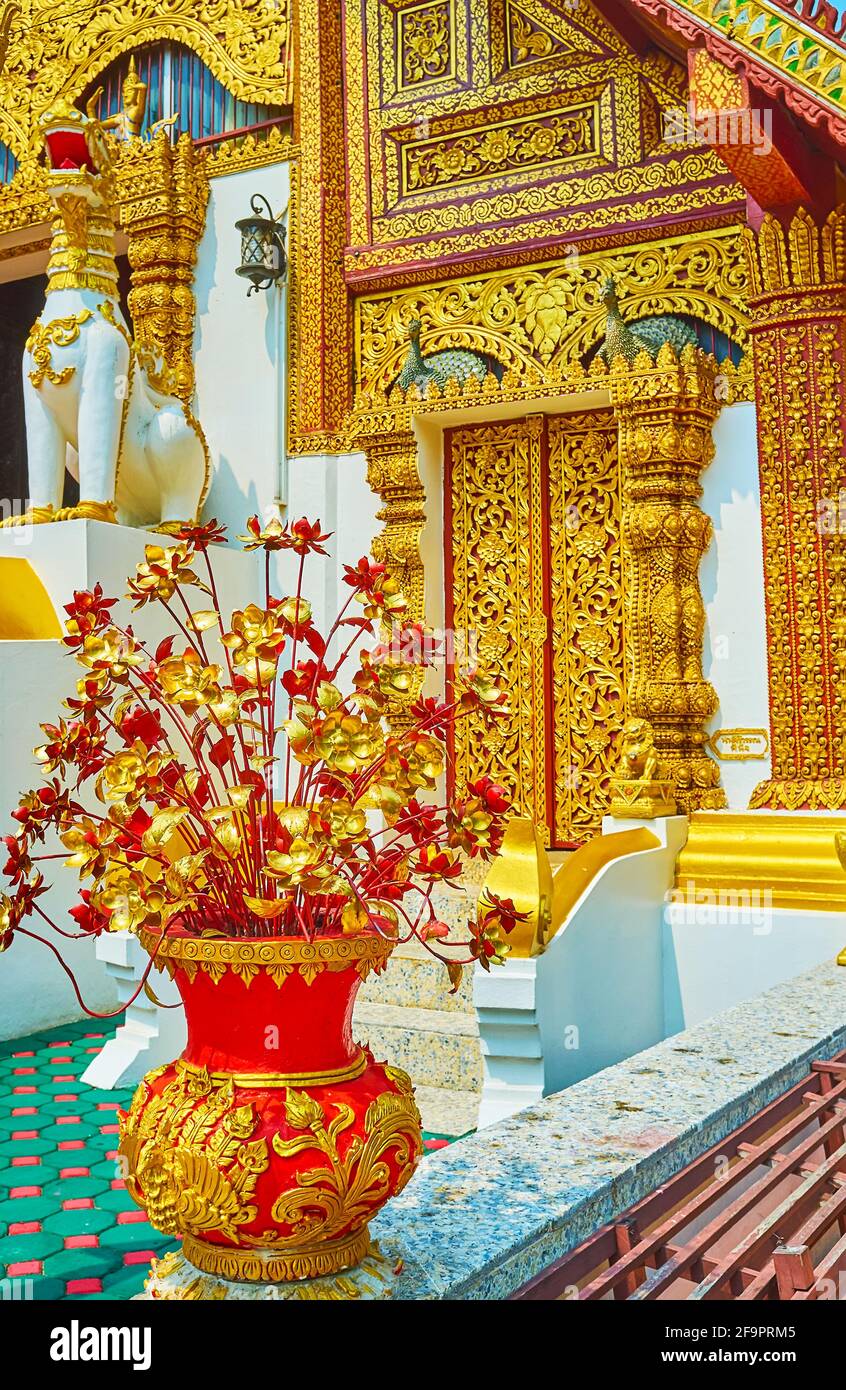 I fiori dorati in vaso rosso brillante con motivi dorati davanti all'Ubosot di Wat Phra Singh, Chiang Rai, Thailandia Foto Stock