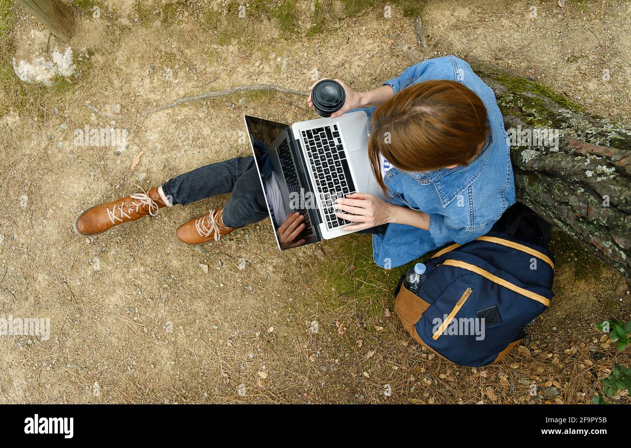 Giovane donna seduta a terra in foresta e che lavora su un computer portatile . Foto Stock