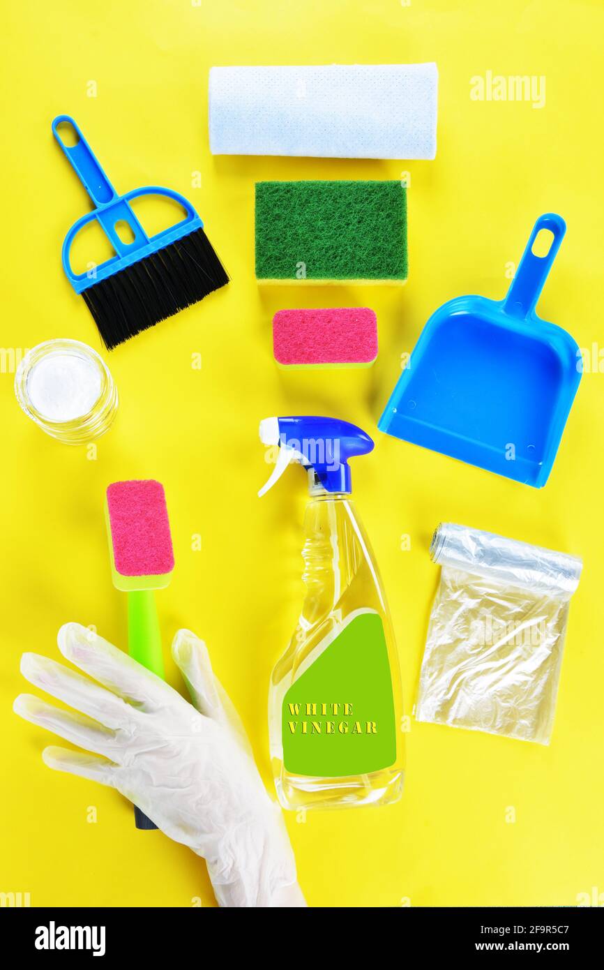 Concetto di pulizia con una mano con guanto, spugne, aceto bianco, bicarbonato di sodio, paletta e. scopa a frusta su sfondo giallo Foto Stock