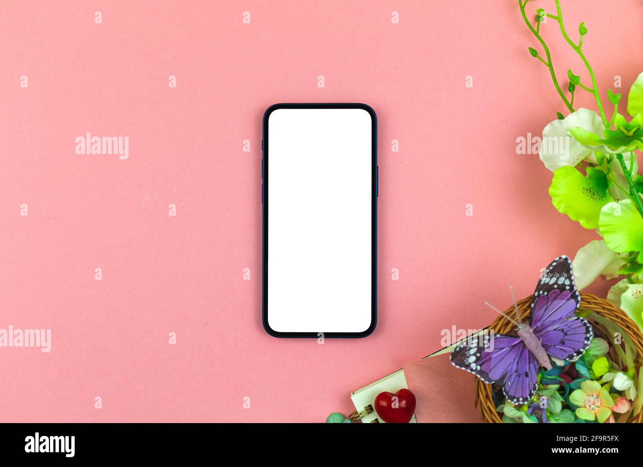 Concetto di mockup del giorno della mamma con schermo bianco vuoto, sfondo moderno dell'area di lavoro con fiori e farfalla, foto dall'alto Foto Stock