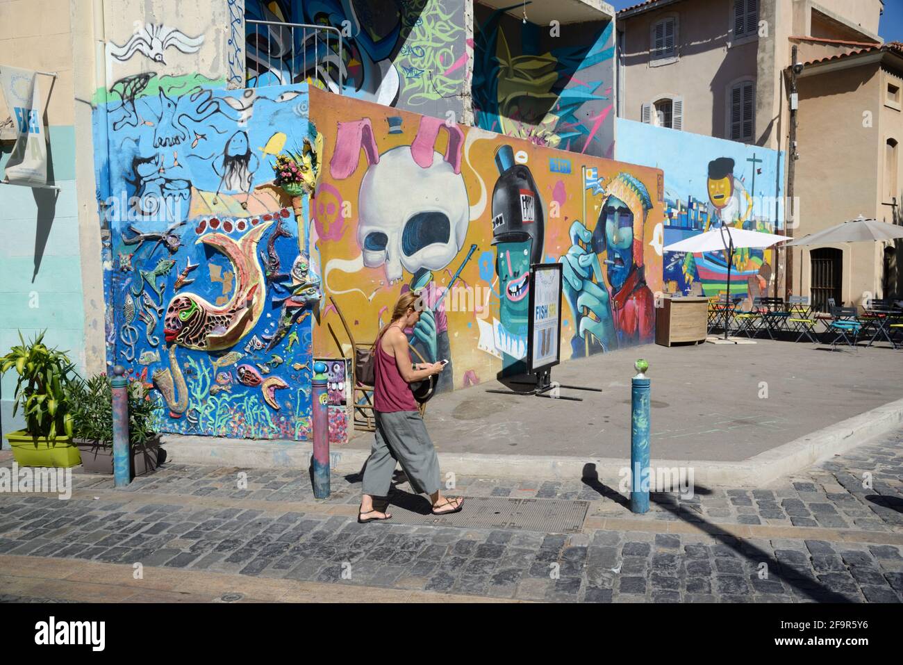 Giovane donna o passeggiate turistiche attraverso la piazza principale, Place de la Charité, e Street Art o pannelli di Graffiti, Panier Città Vecchia Marsiglia Francia Foto Stock