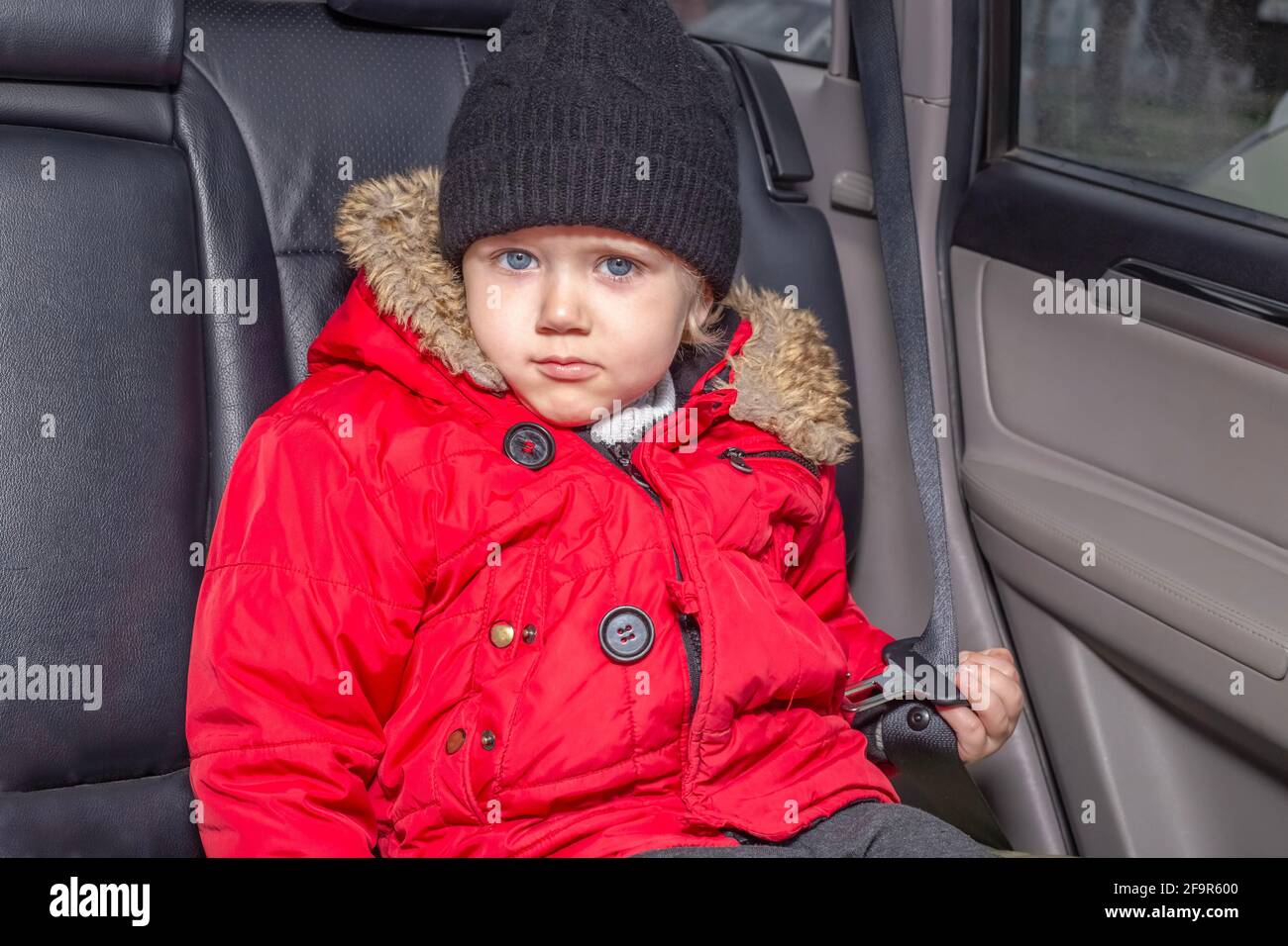 Trasporto di bambini piccoli in auto. Un ragazzo in una giacca rossa si siede nell'abitacolo di un'auto non dotata di un sistema di ritenuta per bambini, hol Foto Stock