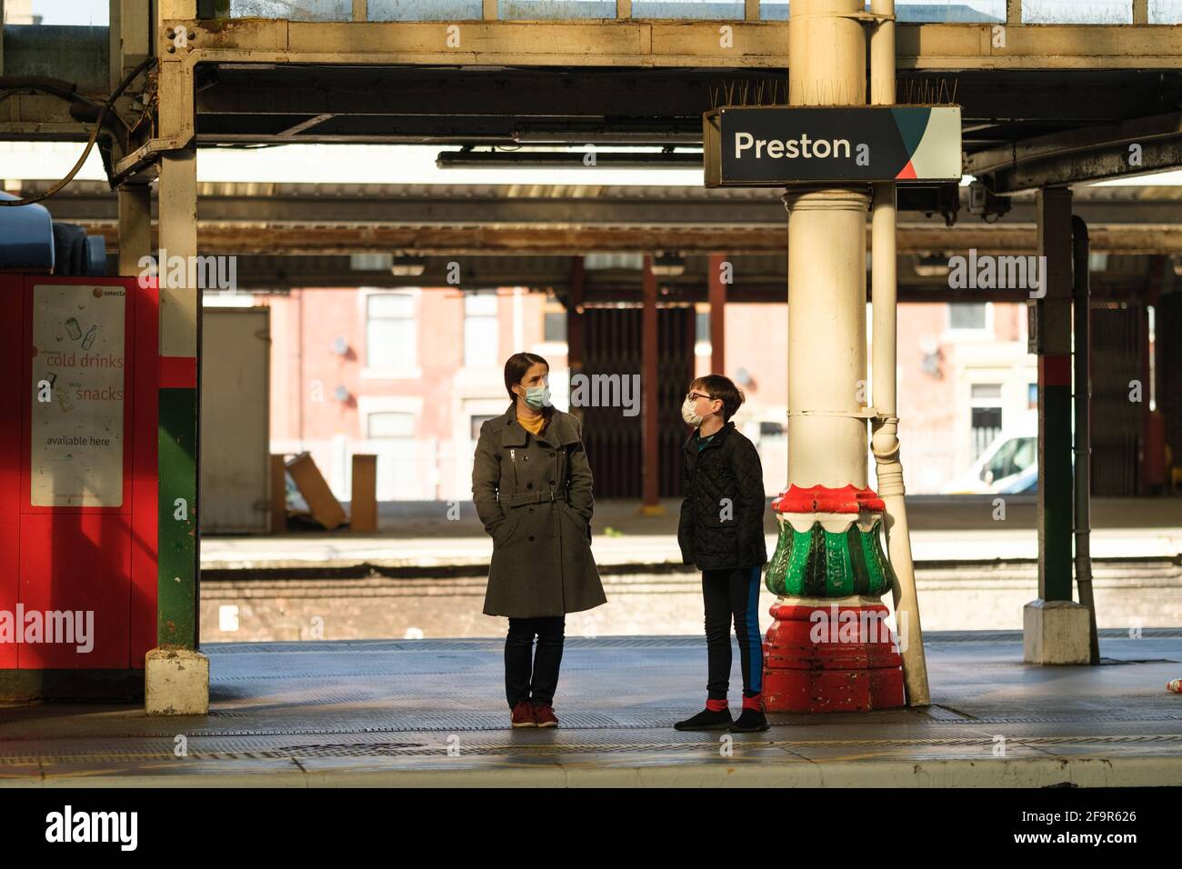 Donna e ragazzo indossano maschere in attesa di un treno alla stazione ferroviaria di Preston, Lancashire, Regno Unito. Foto Stock