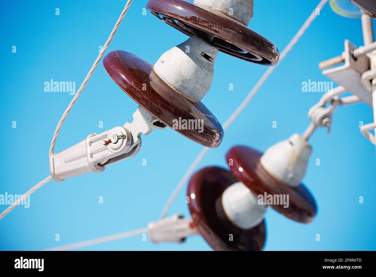 Un isolante sospeso in ceramica è sospeso da una linea di alimentazione contro un cielo blu. Primo piano. Foto Stock