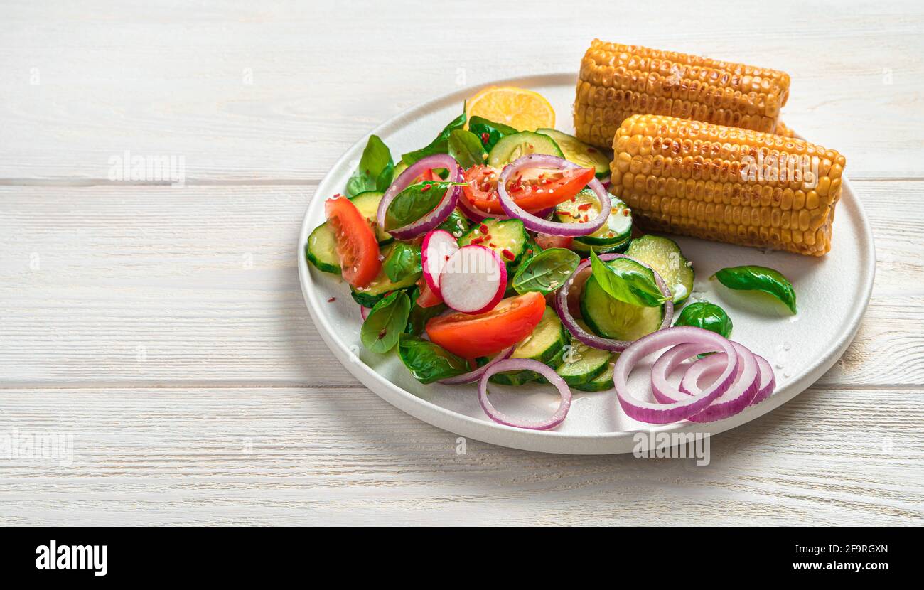 Insalata fresca con verdure e mais su un piatto bianco piatto su uno sfondo chiaro con spazio da copiare. Vegetariano, cibo dietetico. Foto Stock