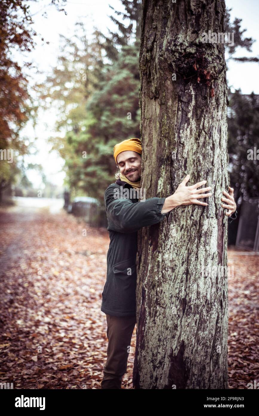 l'uomo amorevole naturale sorride e abbracci albero su foglia coperta via berlino Foto Stock