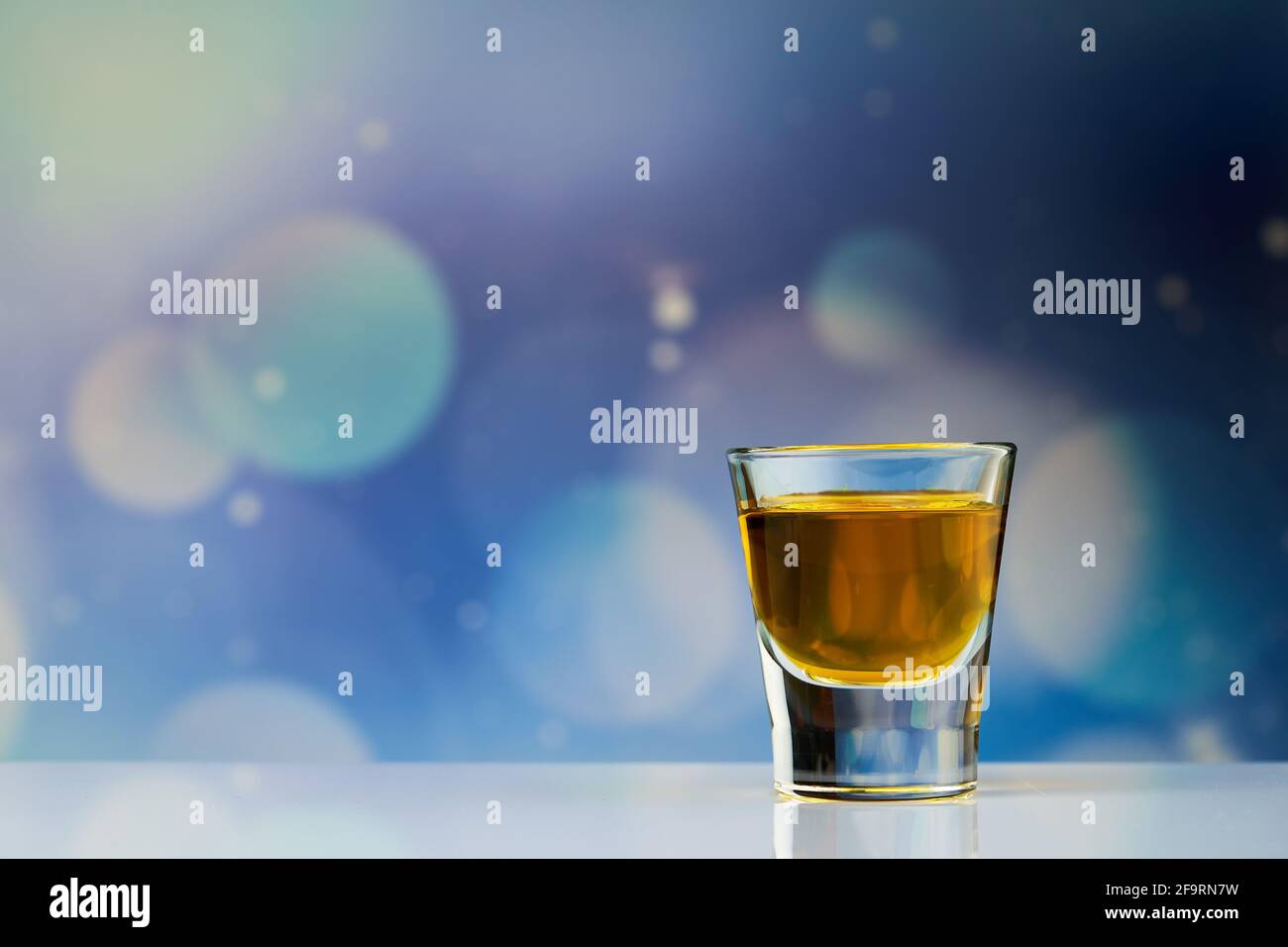 Bevanda gialla all'interno del piccolo shot sullo sfondo blu. Foto Stock