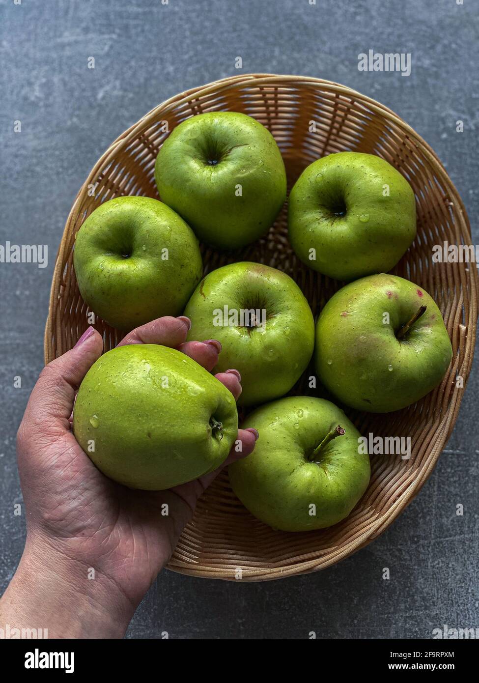la mano tiene una mela sullo sfondo di un cestino con mele Foto Stock