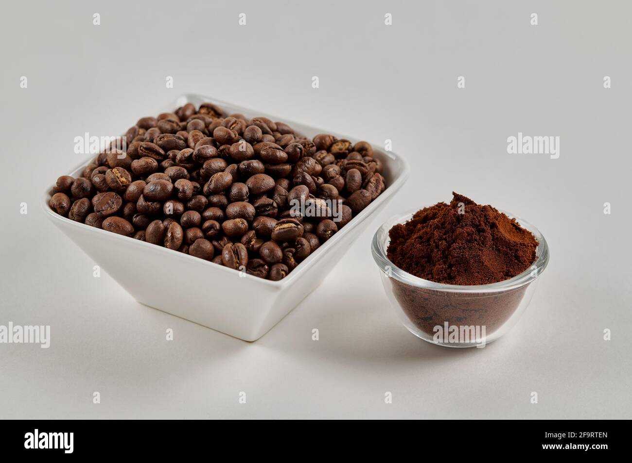 Chicchi di caffè interi alla pesciolina e polvere di caffè appena macinata su sfondo bianco Foto Stock