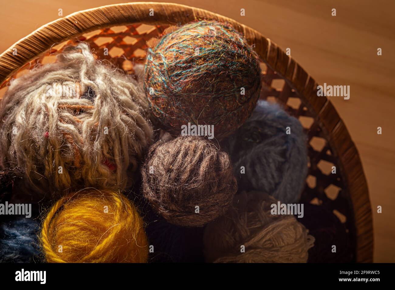 Primo piano dei materiali di consumo per la lavorazione a maglia. Palle di lana di maglia in un cesto rotondo di vimini. Foto Stock