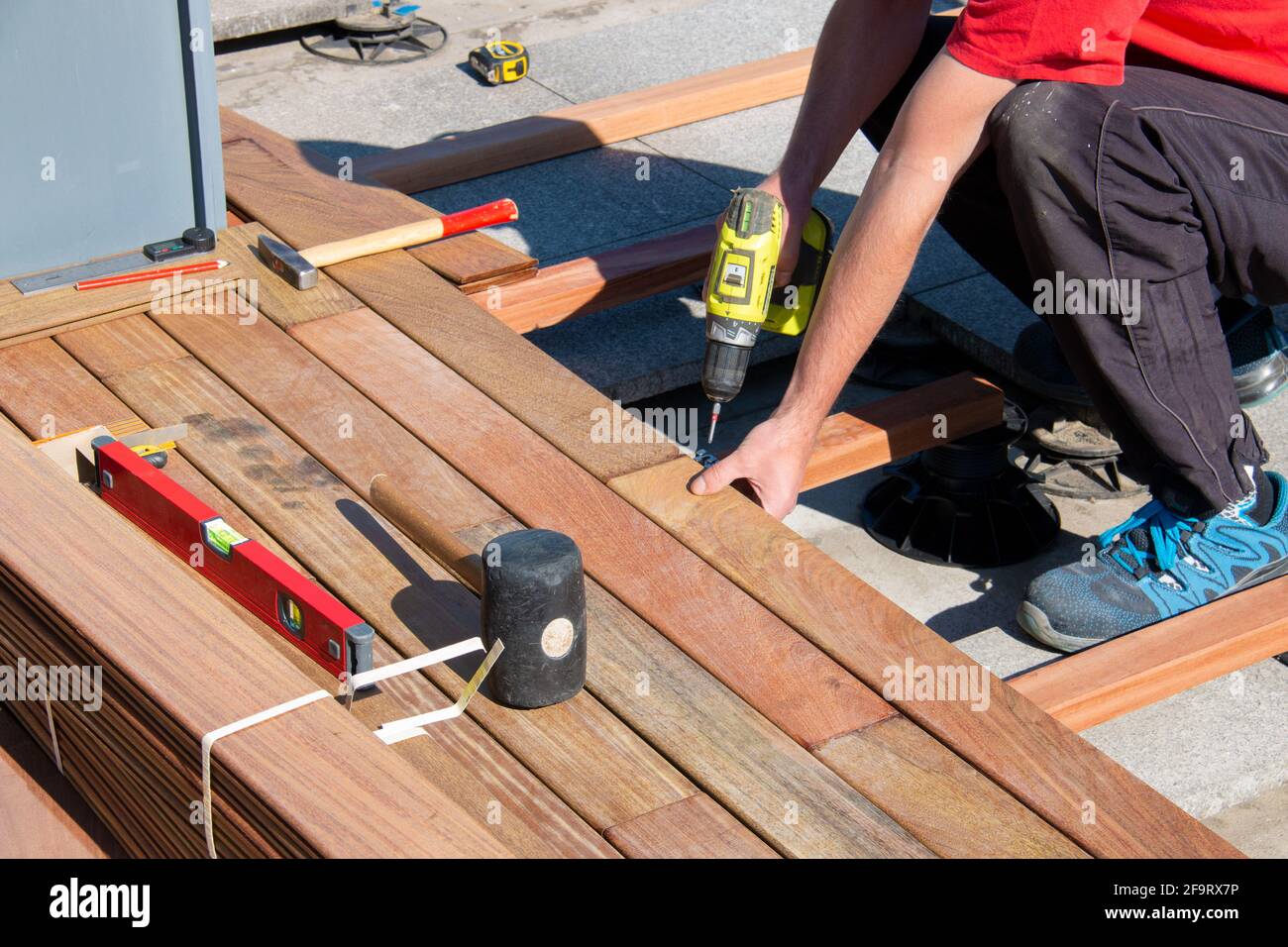 Costruzione di terrazzo di legno duro - uomo che lavora duro che installa legno esotico di ipe che fa da ponte tavole di legno, pavimenti residenziali Foto Stock