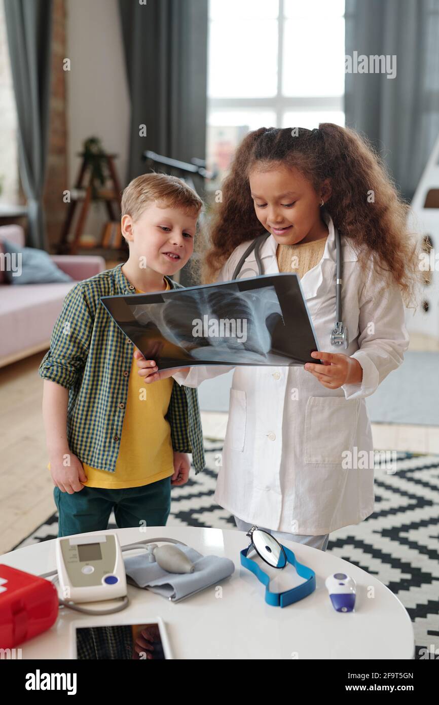 Due bambini che esaminano l'immagine radiografica insieme durante il loro gioco ospedale a casa Foto Stock