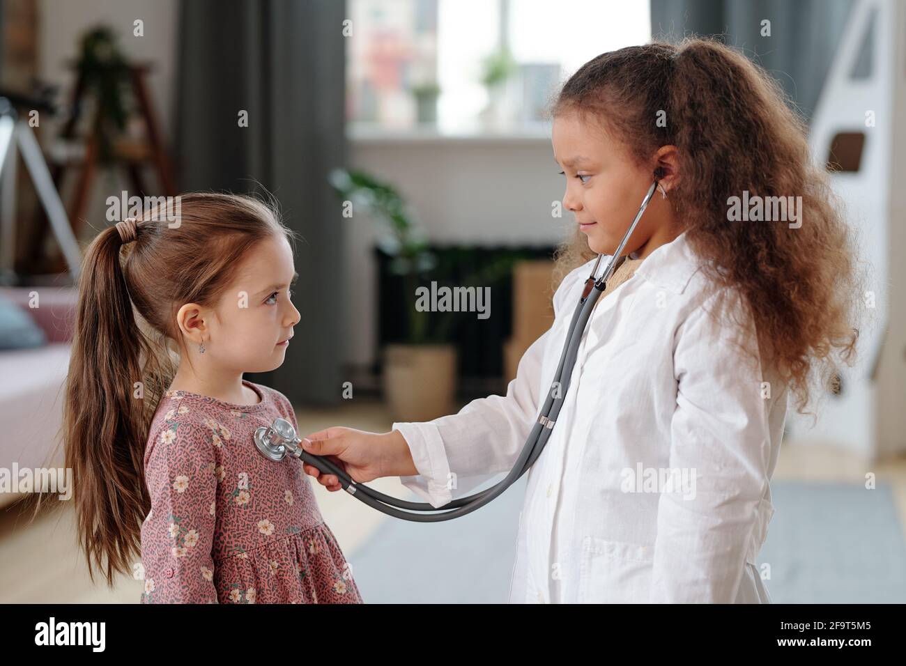 Ragazza che gioca in medico e ascoltando il battito del cuore di lei poco paziente mentre giocano a casa Foto Stock