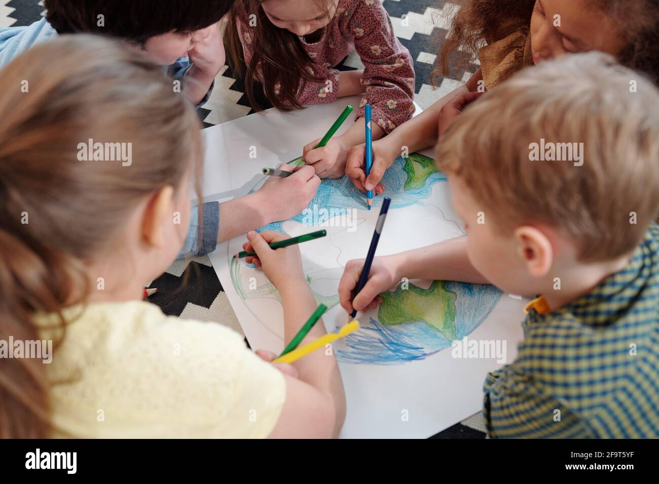 Gruppo di bambini seduti al tavolo e disegnando un immagine con matite colorate insieme Foto Stock