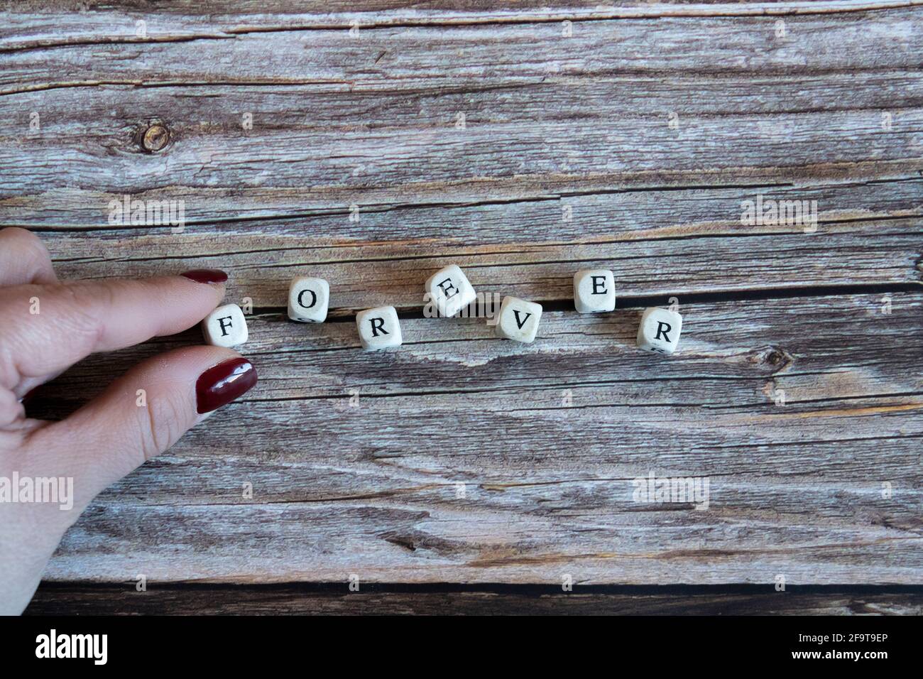 Le dita delle donne che mettono dadi che formano la parola 'per sempre' su uno sfondo di legno. Spazio di copia Foto Stock