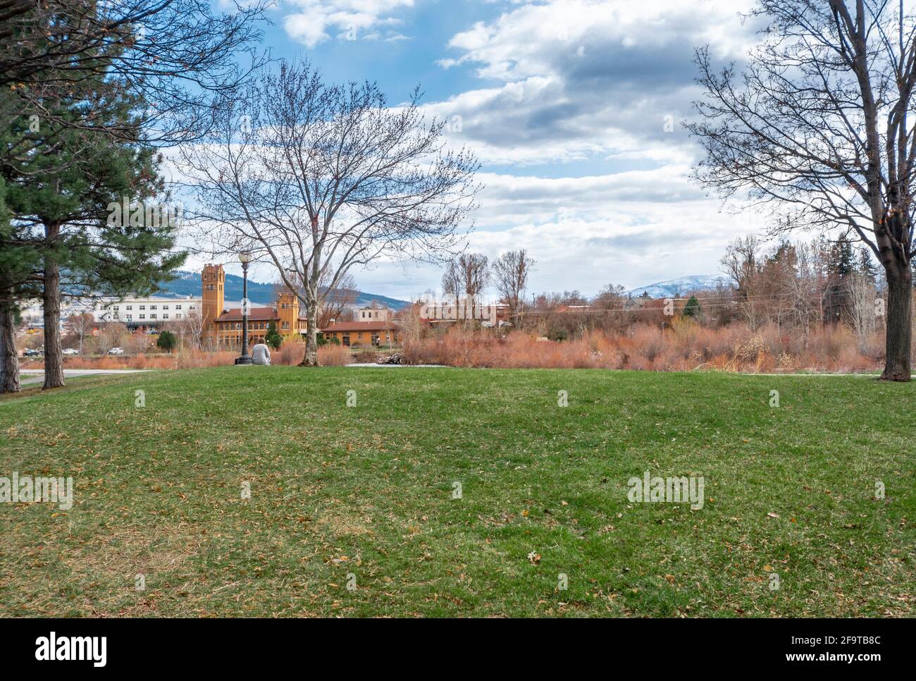 Una donna si rilassa in un parco pubblico lungo il fiume Clark Fork con il centro di Missoula, Montana, USA visto in lontananza. Foto Stock