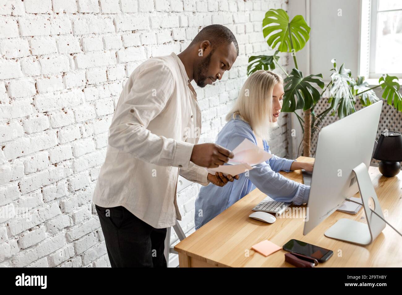 Colleghi di gara misti utilizzando il computer, facendo alcuni documenti, l'apprendimento di grafici finanziari. Giovani colleghi di stile che discutono nuove idee per il progetto Foto Stock