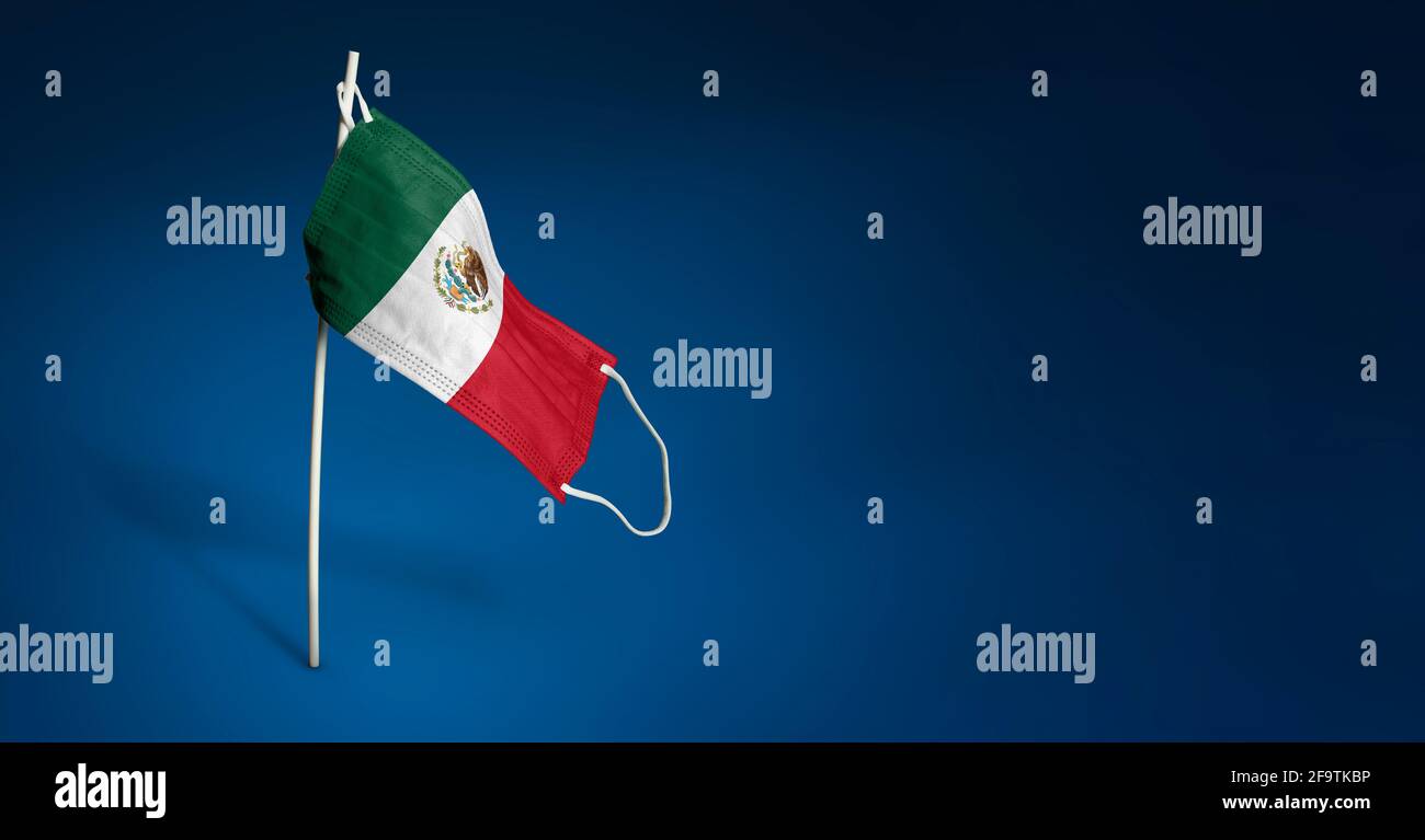 Maschera Messico su sfondo blu scuro. Bandiera sventolante del Messico dipinta su maschera medica sul palo. Flag di attacco del virus. Concetto della bandiera della lotta agai Foto Stock