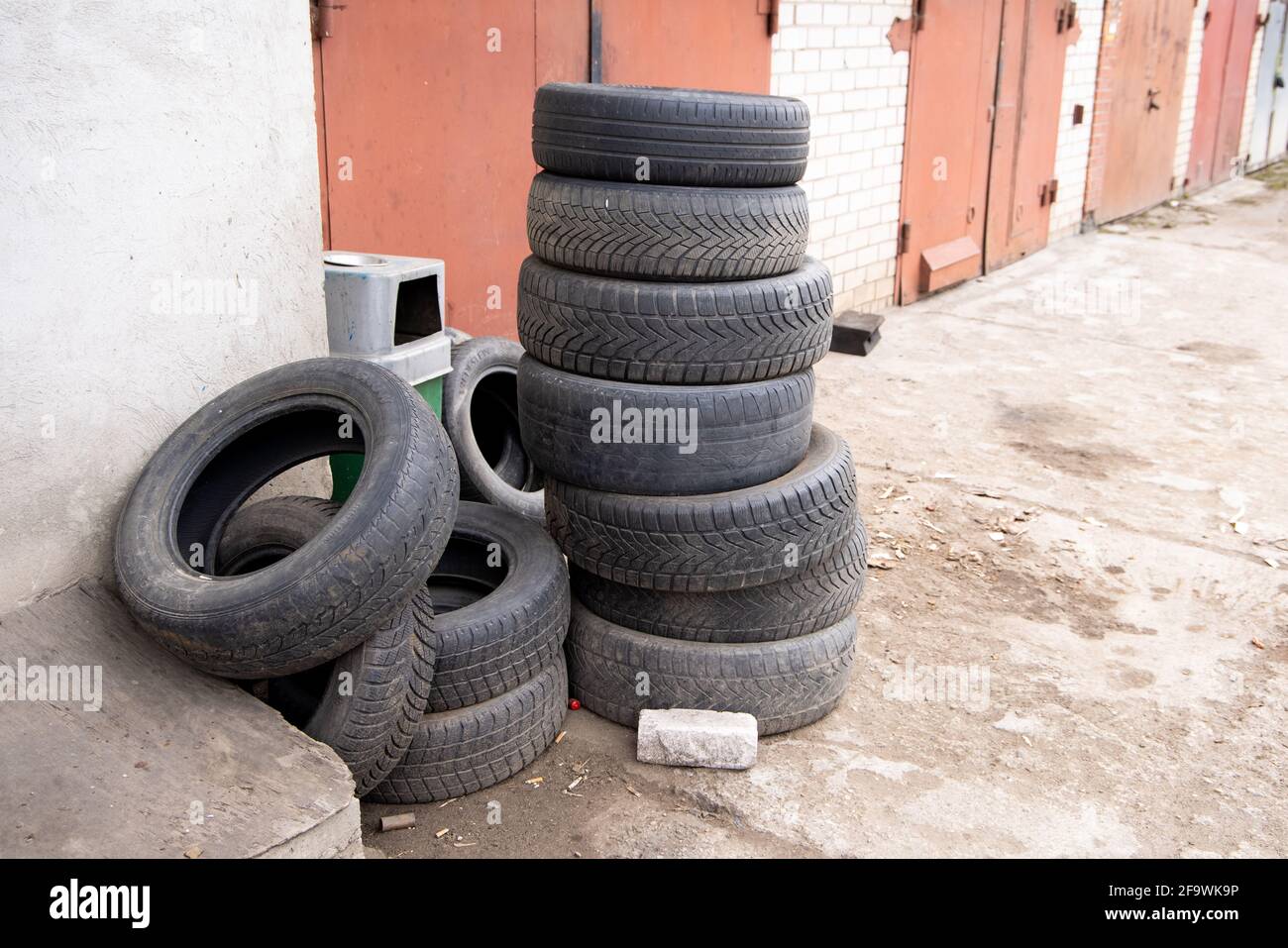 Pila di vecchi pneumatici auto contro il muro di mattoni di servizio pneumatici o garage. Inquinamento, riciclaggio e riscaldamento globale. Foto Stock