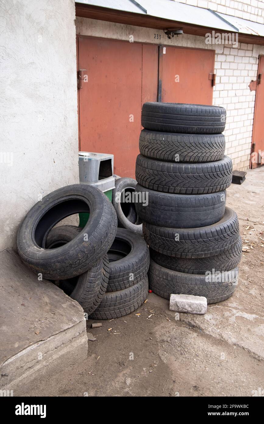 Pila di vecchi pneumatici auto contro il muro di mattoni di servizio pneumatici o garage. Inquinamento, riciclaggio e riscaldamento globale. Foto Stock