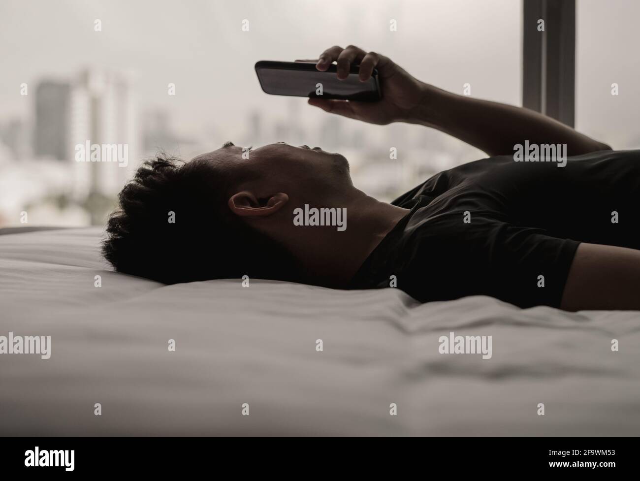 L'uomo asiatico si sente triste sul letto guardando e concentrarsi sullo smartphone. Internet concetto di dipendenza dai social media e di salute mentale. Foto Stock