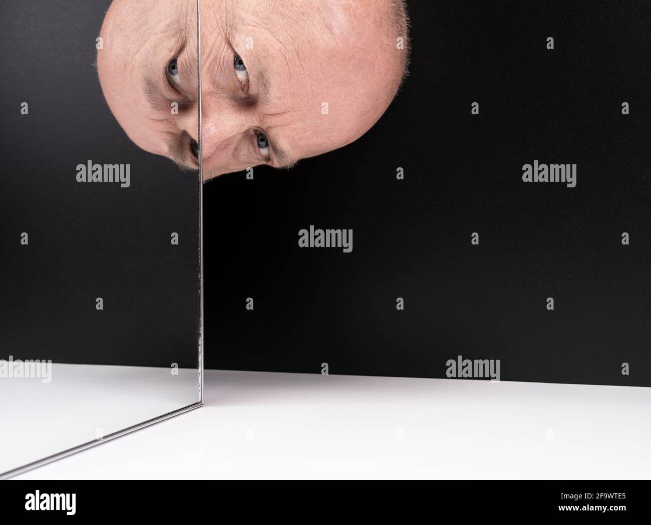 un uomo di mezza età guarda da dietro uno specchio Foto Stock