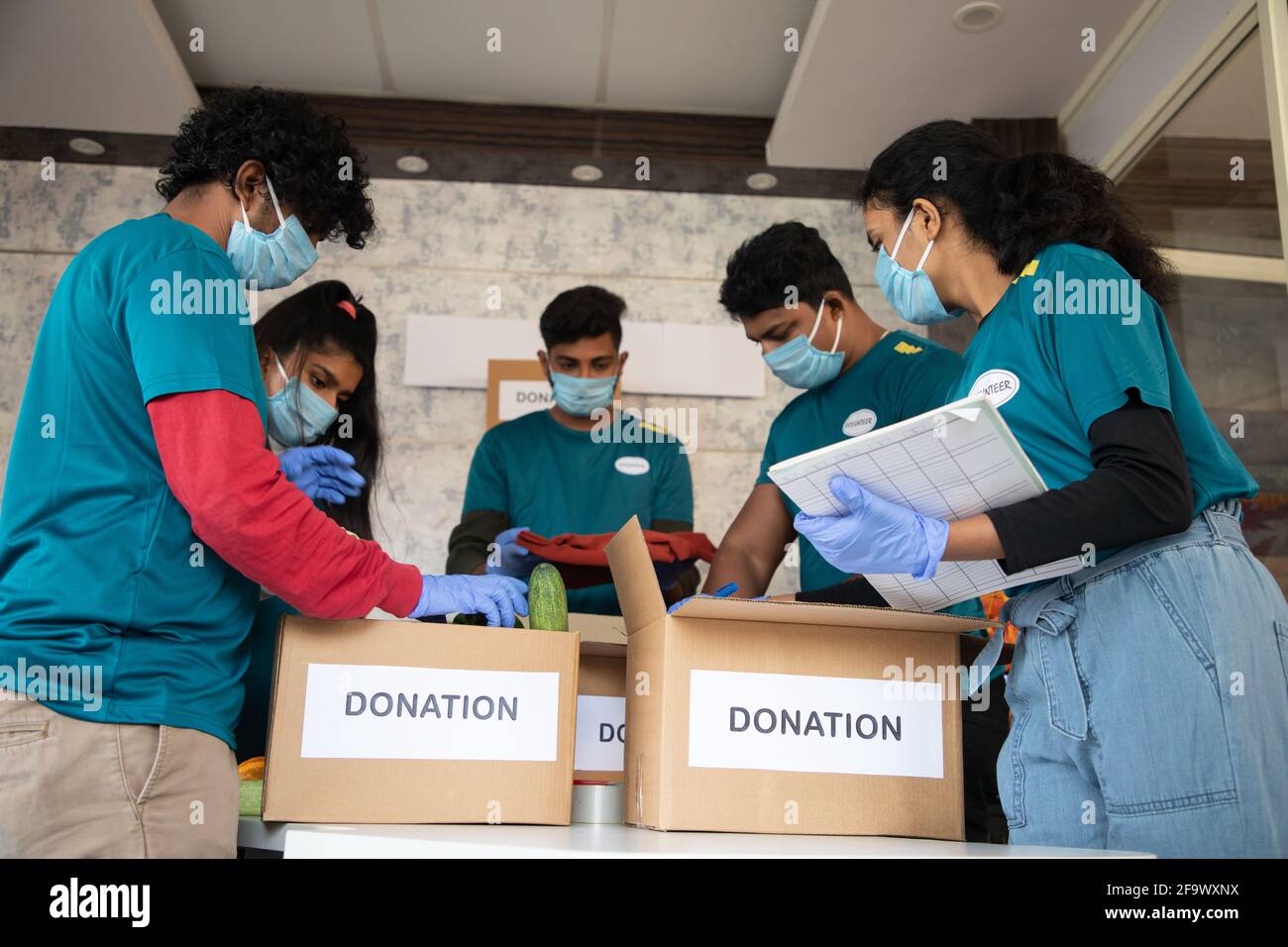 Vista ad angolo basso, gruppo di volontari impegnati a lavorare organizzando verdure e vestiti su scatole di donazione e annotando durante il Coronavirus covid-19 Foto Stock