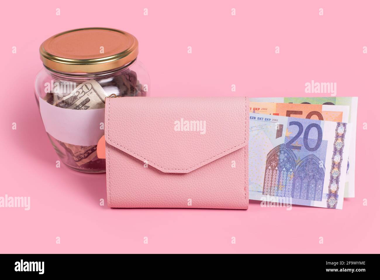 Dollari americani in vaso di vetro con etichetta vuota e portafoglio rosa pieno di banconote in euro, finanziario, risparmio, cambio, diversificazione. Vaso pieno di Foto Stock