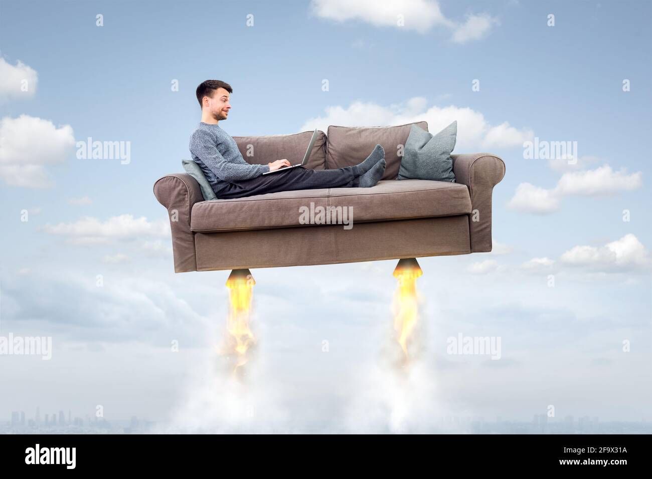 Un uomo che vola su un divano a razzo mentre usa un computer portatile Foto Stock
