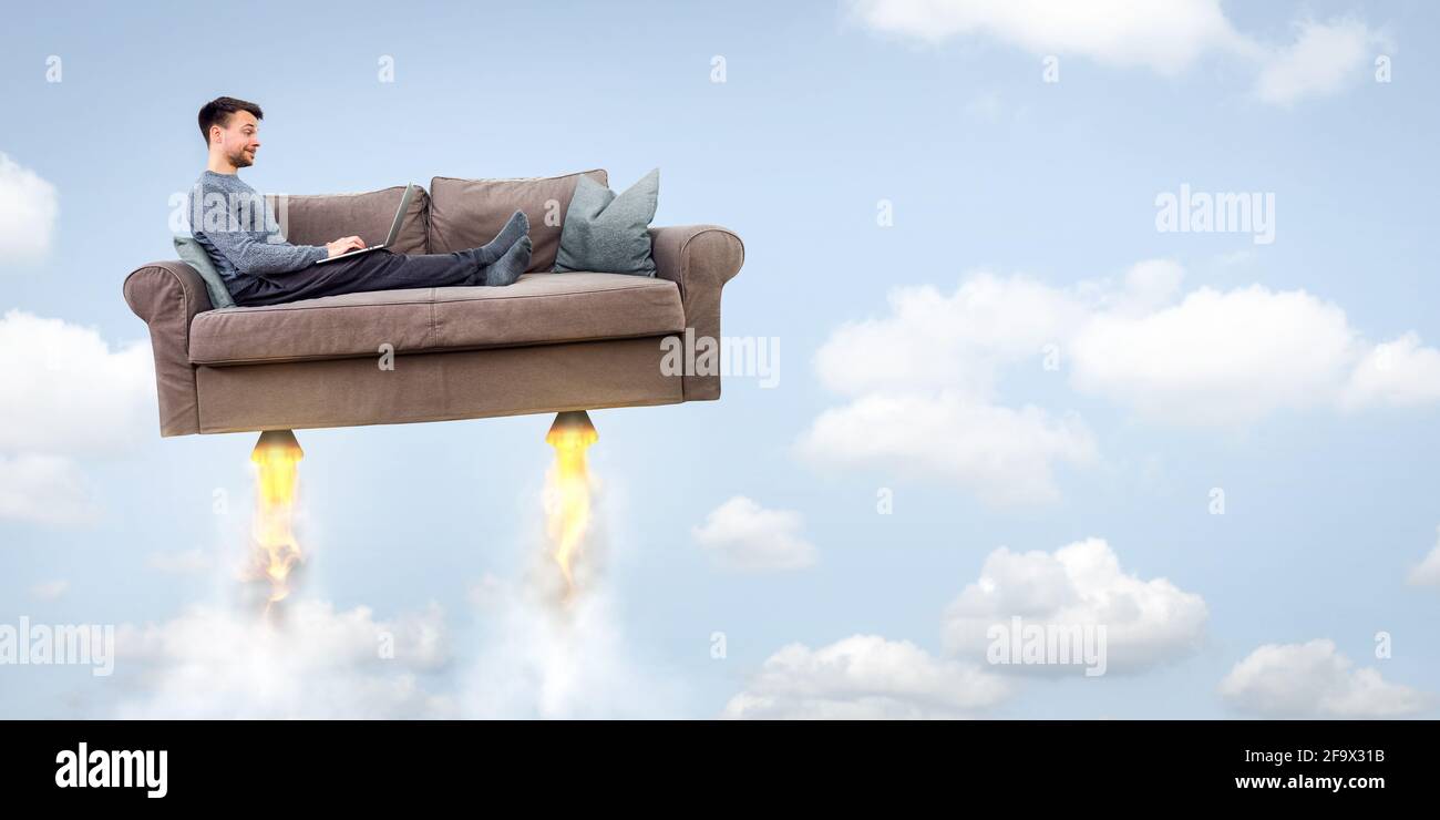 Un uomo che vola su un divano a razzo mentre usa un computer portatile Foto Stock