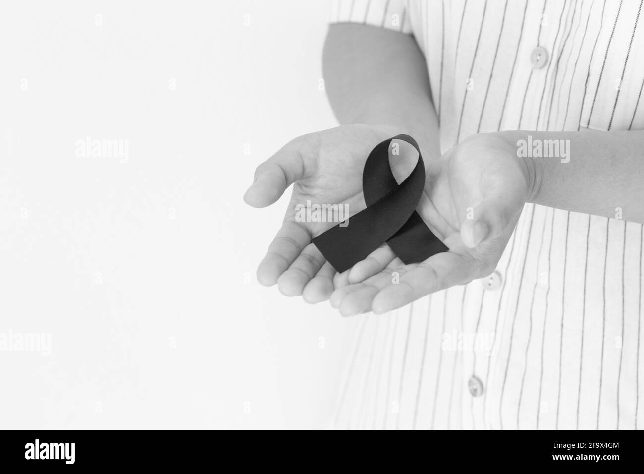 Mano che tiene nastro nero su sfondo bianco con spazio di copia, simbolo del mese di consapevolezza del cancro della pelle il mese di maggio, cancro del melanoma, nastro di lutto simbolico Foto Stock