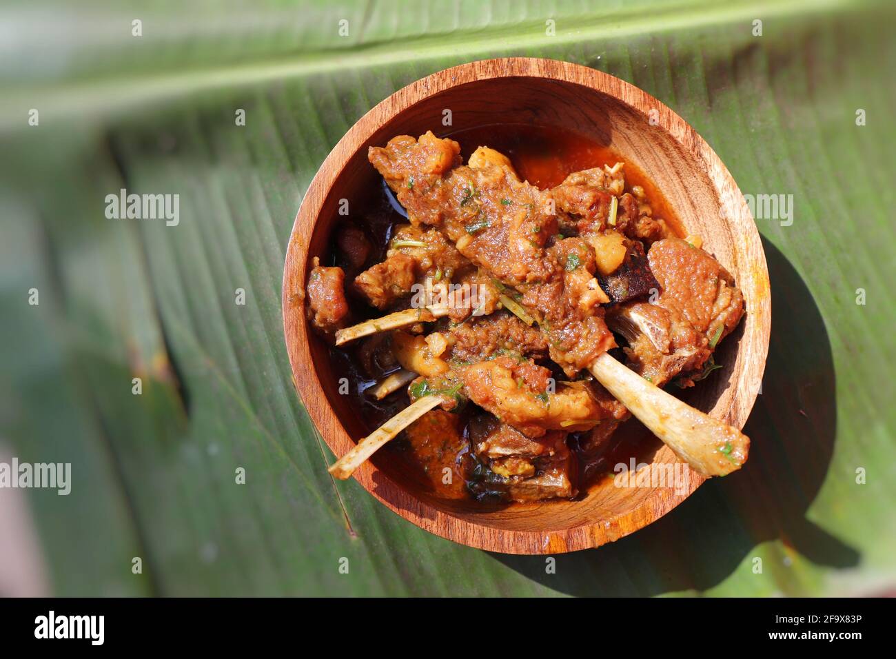 Mutton trita il curry. Curry di capra rustico indiano piccante non vegetariano. Servito in una ciotola di legno su uno sfondo di foglia di Banana. Spazio di copia. Foto Stock