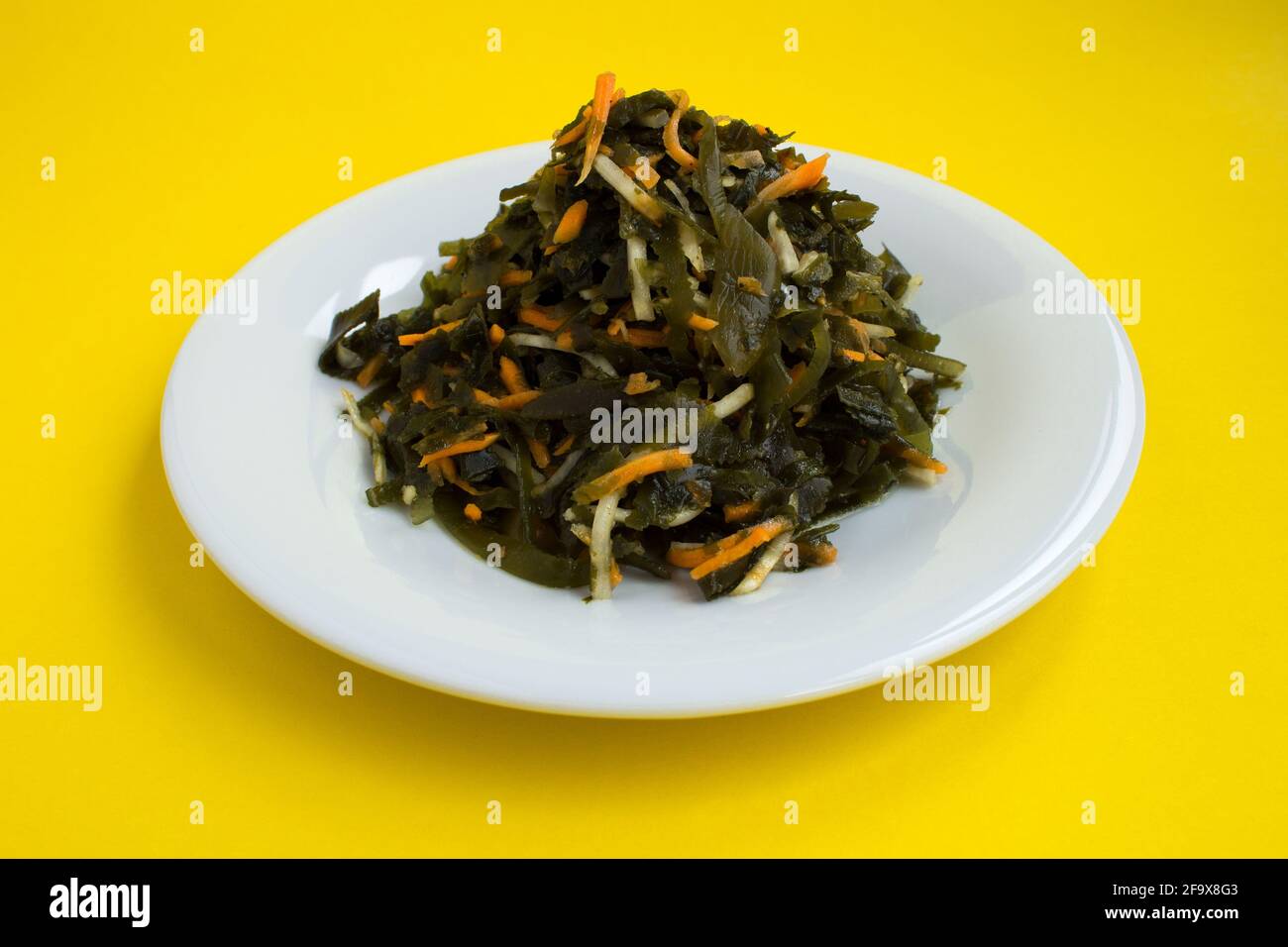 Insalata con alghe, sedano e carote nel piatto bianco su sfondo giallo Foto Stock