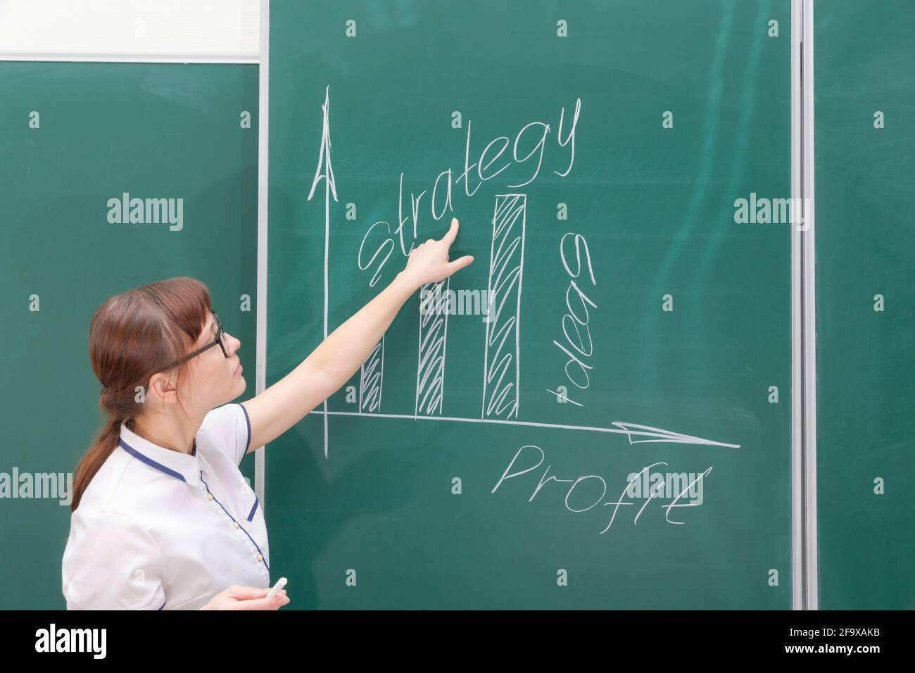 una giovane vettura di affari della donna in una blusa bianca e gli occhiali mostrano con la sua mano un diagramma di costruzione di un commercio su un lavoro di ufficio di graph Foto Stock