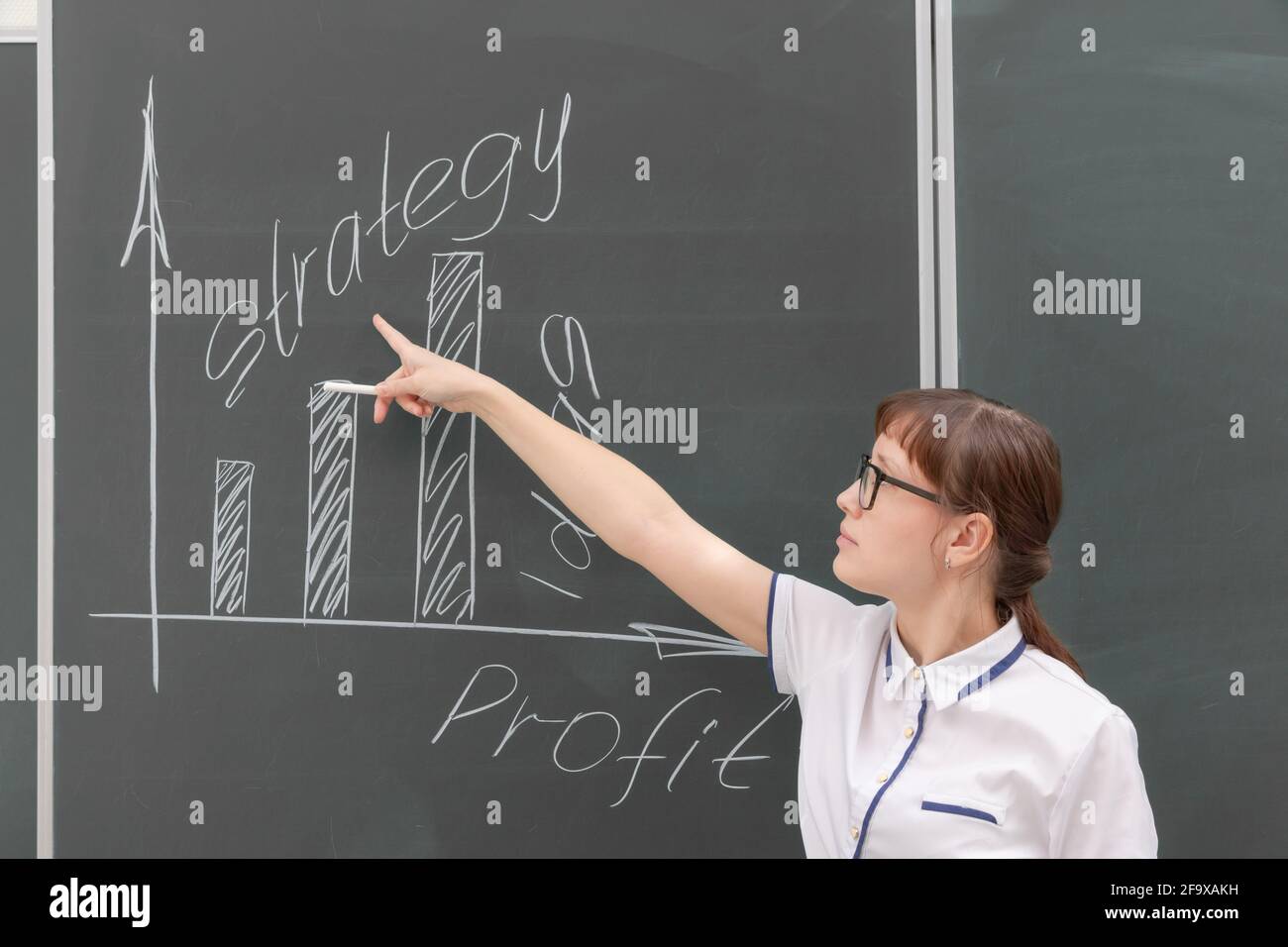 una giovane vettura di affari della donna in una blusa bianca e gli occhiali mostrano con la sua mano un diagramma di costruzione di un commercio su un lavoro di ufficio di graph Foto Stock